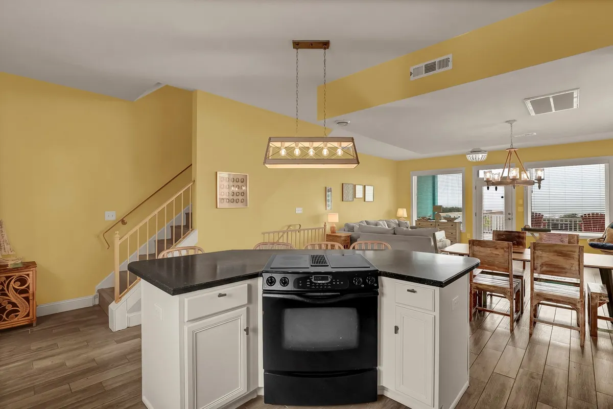 A modern kitchen space highlighting a prominent kitchen island, a sleek black stove, a dining area in the background, and large windows that flood the room with light. The setup encourages cooking, dining, and socializing in a warm, welcoming environment.
