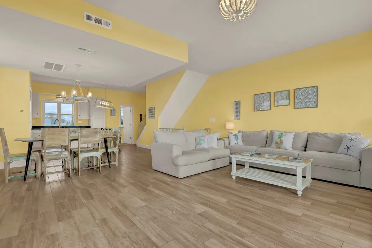 A spacious interior room with a cozy sofa, a family-sized dining table beneath a chandelier, and sunny yellow walls. The setup encourages gathering, dining, and sharing special moments, while feeling bright and welcoming.