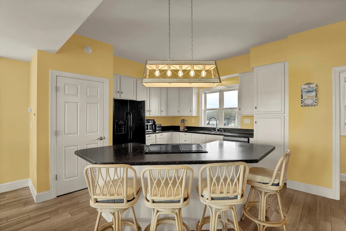 A bright and airy kitchen featuring a large island countertop with comfortable bar stools, stylish pendant lighting, and expansive windows that let in plenty of natural light. The space is open and inviting, perfect for preparing meals, entertaining, or gathering with family.