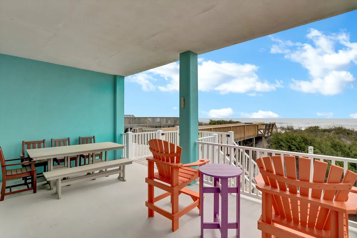 An outdoor dining space featuring colorful chairs and a table set against a backdrop of the sea. The view invites relaxation and socializing, with the balcony clearly offering a seamless indoor-outdoor connection.