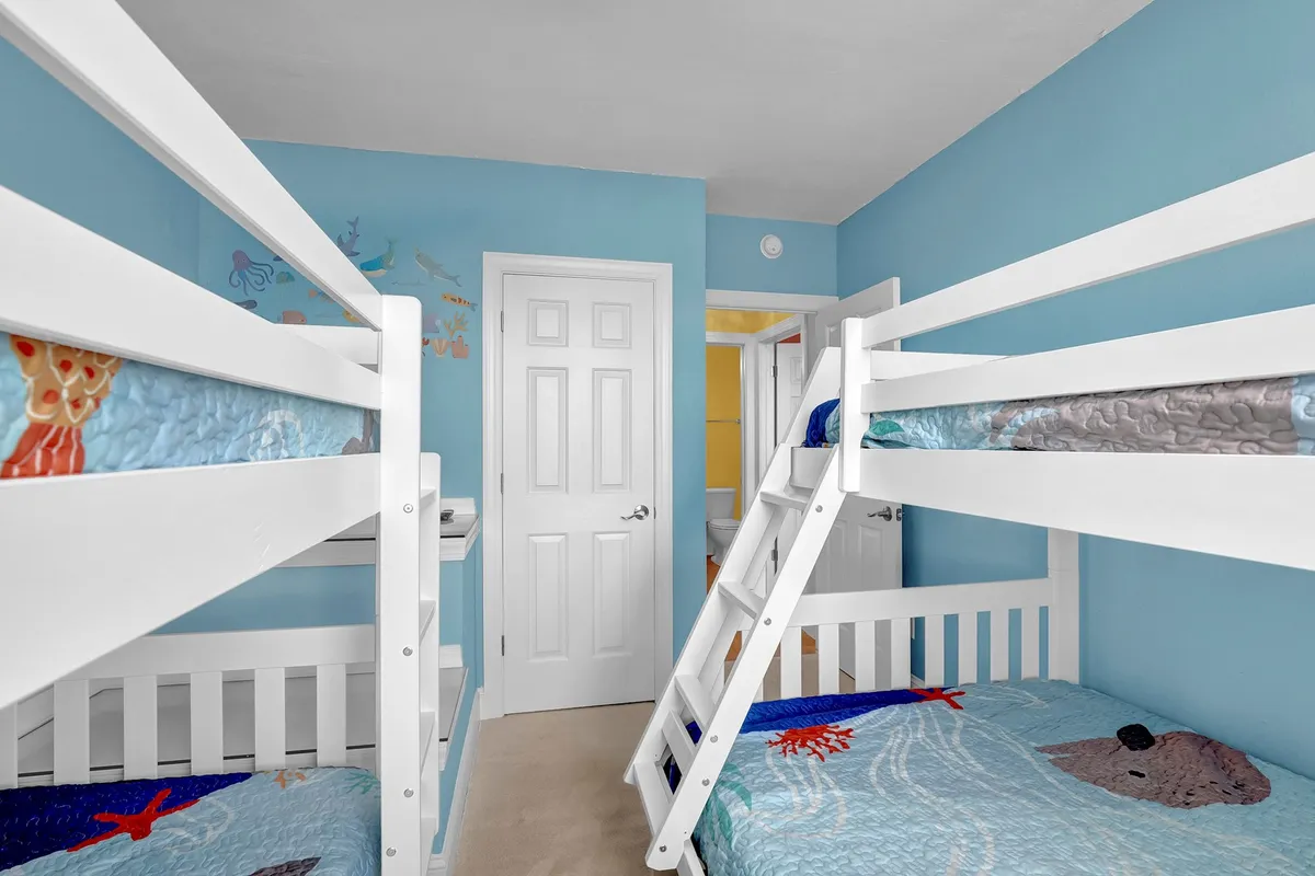 A playful bunk room featuring two bunk beds with colorful bedding, whimsical wall decorations, and ample space for kids or teens to sleep and play. The decor inspires imagination and fun while prioritizing comfort.