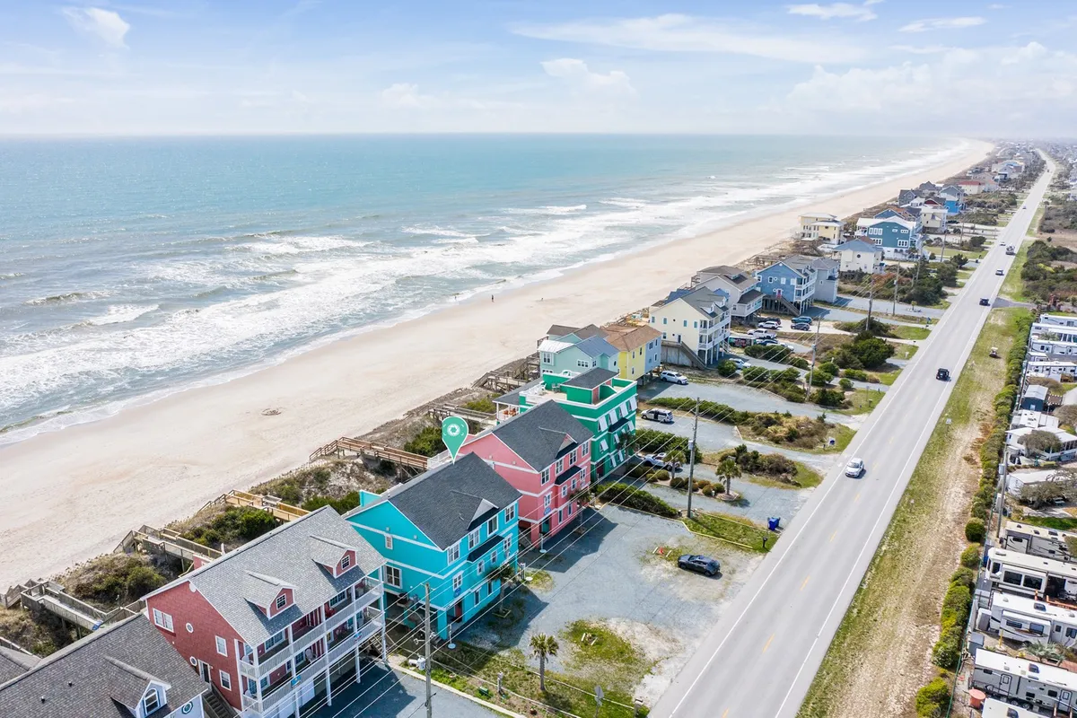 A sunny, inviting scene of colorful beach houses lining the shore, with ocean waves gently lapping the sandy beach and a coastal road running parallel to the shoreline. The atmosphere is tranquil, perfect for romantic strolls or watching the sunrise together.