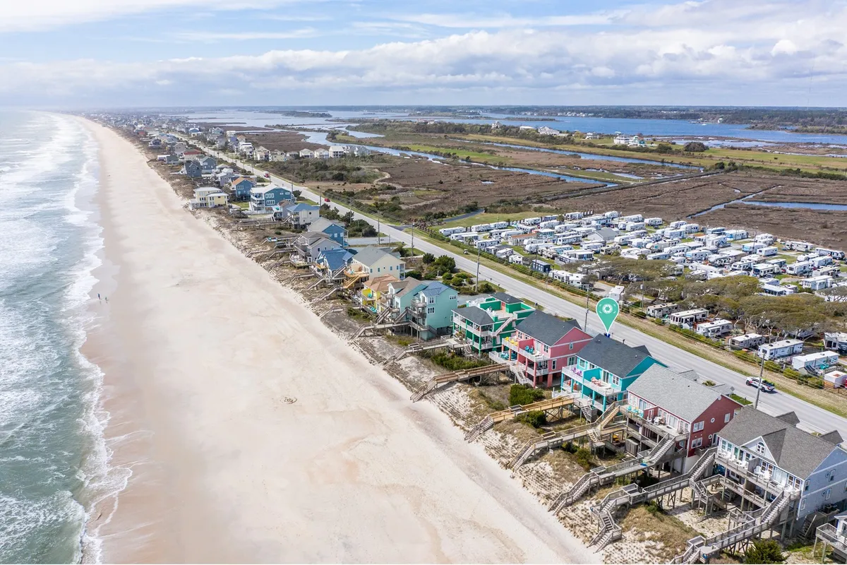 A sweeping view of beachfront properties with ocean waves rolling in, a coastal road curving along the shoreline, and green marshland in the distance. The image embodies the freedom of exploring coastal landscapes and returning to a well-situated base.