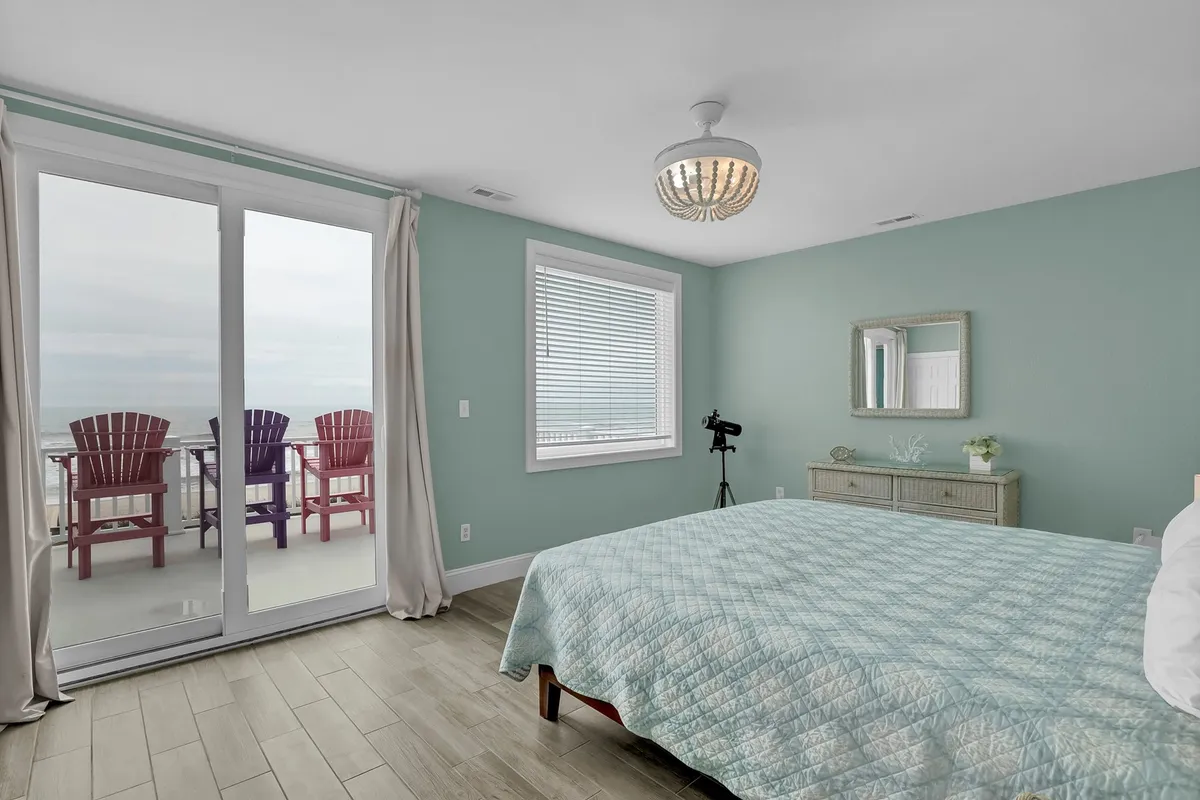 A serene bedroom with a plush King bed, large sliding doors opening to a private balcony with Adirondack chairs, and a telescope for stargazing. The space is bathed in natural light, creating a tranquil atmosphere perfect for relaxation and privacy.